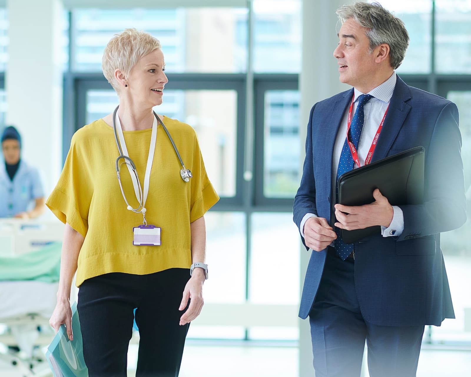 A clinician with a stethoscope and a business advisor walking through a hospital