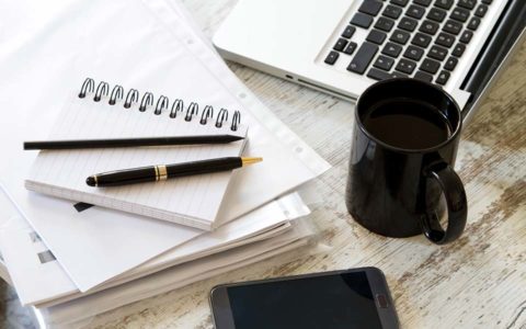 Laptop, notebook with pen, business documents and coffee mug on desk