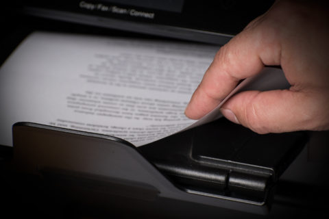 Hand grabbing printed sheets from printer output tray