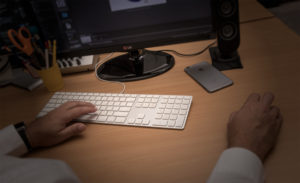 Hands on iMac keyboard showing desk, iPhone and monitor stand base