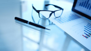 closeup of pen, glasses and printed charts on desk