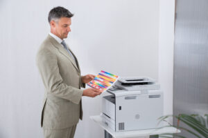 Side view of businessman looking at multi colored paper by color printer in office