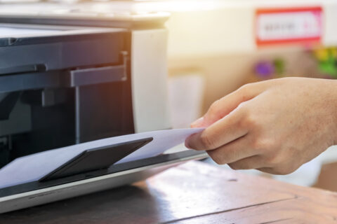 Using the printer. Hand holding paper after printing finished. It is an important device in the office.