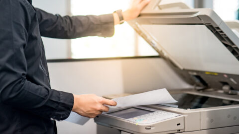 Male businessman using photocopier for copying and printing report paperwork in office. Electronic equipment and supply for business organization.