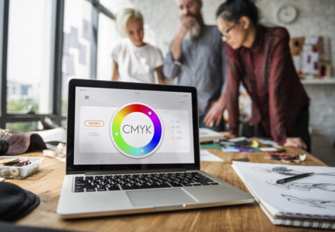 Team of designers working in background with prominent laptop displaying Colour CMYK settings