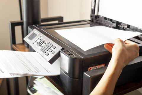 Concept image for office work. A woman is placing or removing paper. There is a wireless photocopier, scanner, printer combo device on top of a shelving unit at a small office setting.