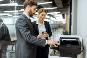 Business man and woman talking near the copier during a coffee break in the hallway of the big corporation