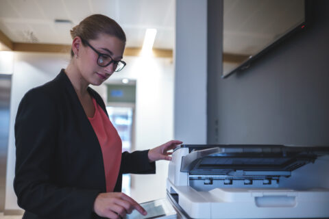 Side view of focused female manager in suit using scanner for making copies of documents while working in modern workspace