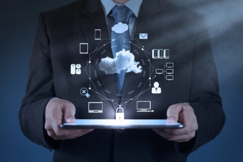 Businessperson holding a laptop mid-camera at waist level with several icons representing cloud services float above it