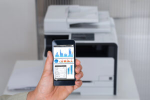 Hand holding cell phone in front of office printer trying to wirelessly print a document