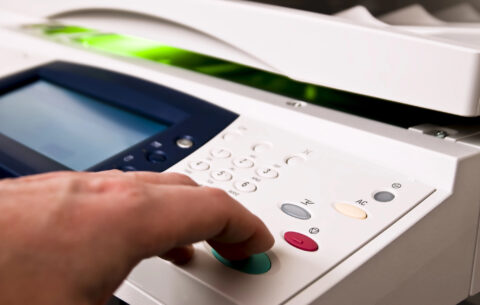 Closeup of a hand pressing the start button on the front panel of an office copier