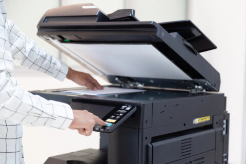Office worker placing a piece of paper on copier glass and pressing button on its control panel