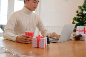 Young man working on laptop in office with Christmas decorations and present visible