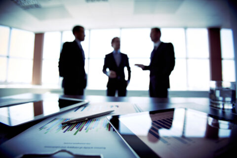 Foreground in an office of business technology and documents with three men out of focus in background