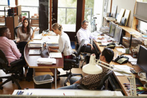 Busy office with workers speaking around a table