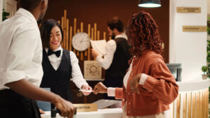 Tourists finishing vacation trip, handing out room card key to cheerful friendly receptionists during check out process. Happy guests preparing to leave hotel after nice stay