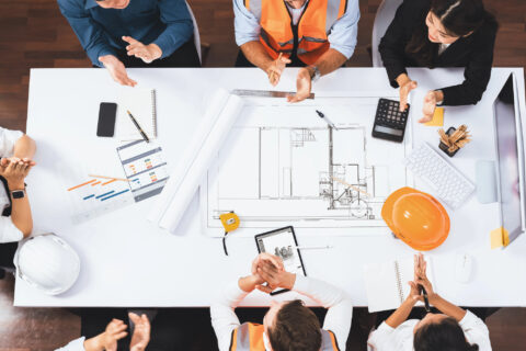 Top view banner of diverse group of civil engineer and clients working together on architectural project, reviewing construction plan and building blueprint at meeting table.