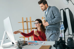 Computer artist pointing out something onscreen to coworker at photo studio