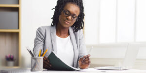 Corporate black businesswoman reviewing documents at her desk in a modern office environment, working diligently.