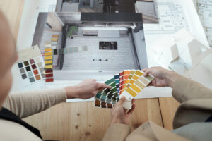 Two persons looking through color swatches over a table containing printouts of architectural renderings.