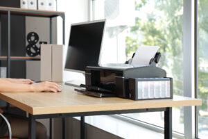 Person working at home with computer and printer on desk by window