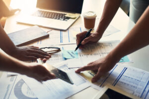 Documents, hands and laptop with business people in office together for accounting or finance. Budget, collaboration and expenses with employee team in workplace for administration or meeting.