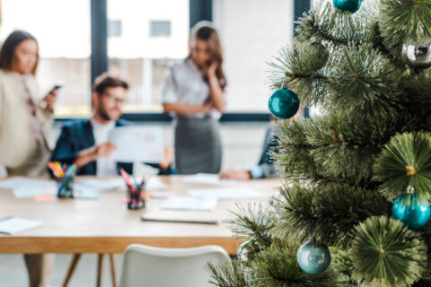 Selective focus of decorated Christmas tree near coworkers in office