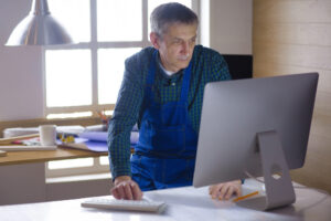 Engineer or carpenter working on laptop and sketching project.