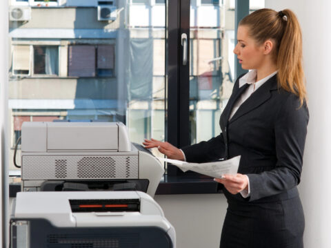 Businesswoman working with a multifunction printer in an office setting.