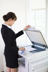 Businesswoman using a multifunction printer, placing a document on the top scanner glass