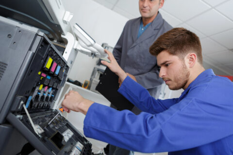 Two repairmen fixing business copier