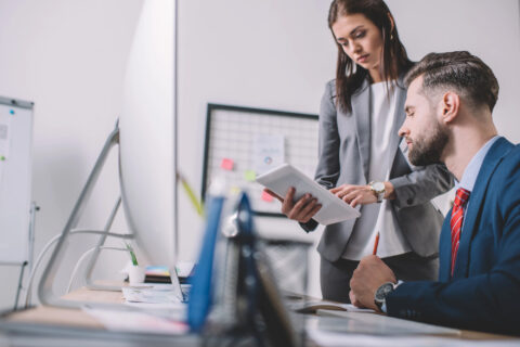 Selective focus of data analyst using digital tablet near colleague at table with computers