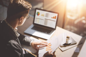 Businessman working at desk comparing a printed report with information on his laptop