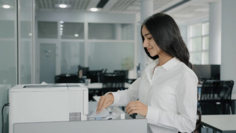 Businesswoman makes copies on photocopier using office equipment print machine papers sending fax printing document press buttons on multifunction printer