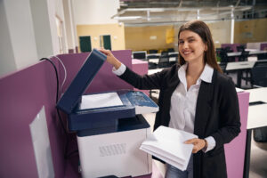 Copier in large shared office space being used by female office worker